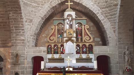 "Chapel with religious cross and alter with yellow and white fabric within a stone building."